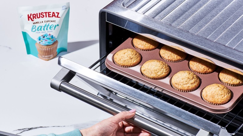 A woman removes a batch of vanilla cupcakes from an oven