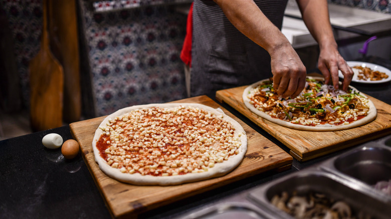 Chef putting toppings on pizza