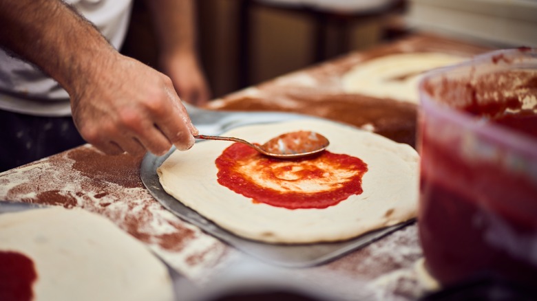 Chef putting sauce on pizza dough