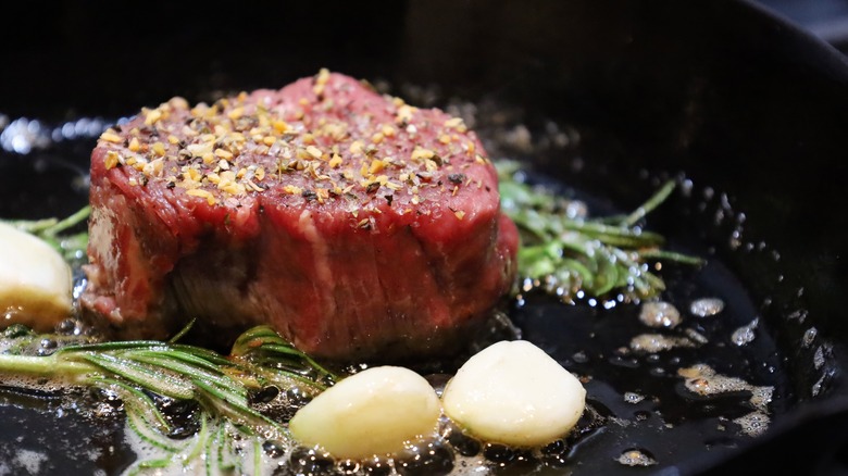 Raw filet mignon in skillet with garlic and herbs