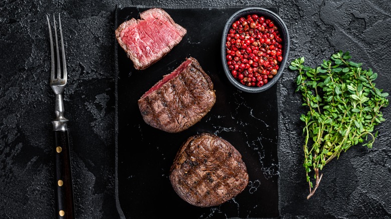 Grilled filet mignon steaks on board with herbs