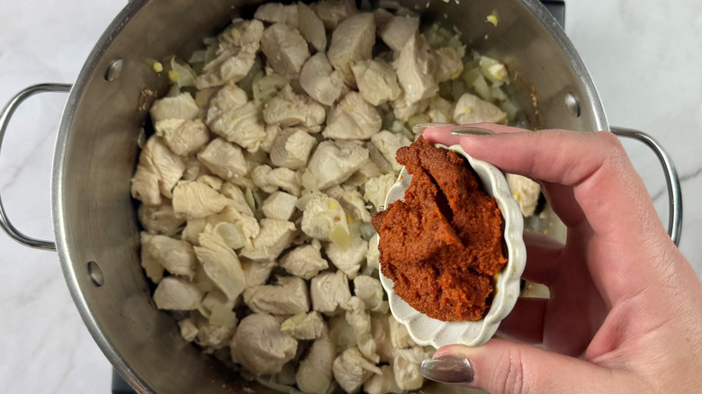 Adding red curry paste to chicken and onions in pot