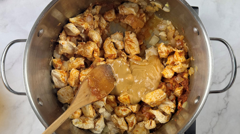 Stirring peanut butter into pot with cooked chicken