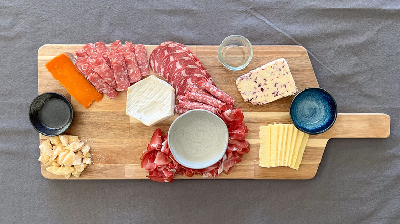 Assorted cheeses, meats, and serving bowls on board