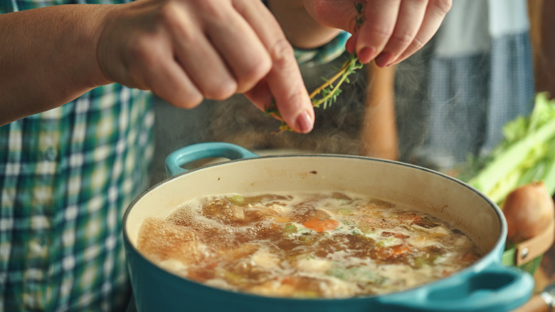 woman adding rosemary to cooking pot