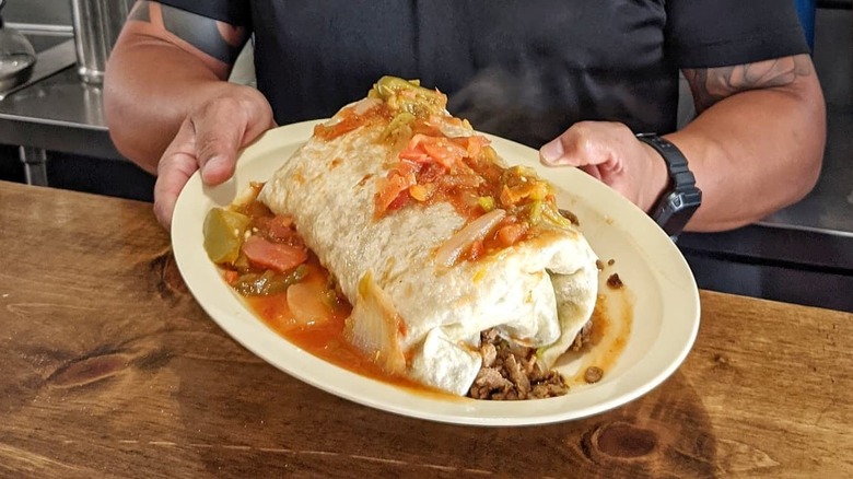 chef holding giant burrito on plate