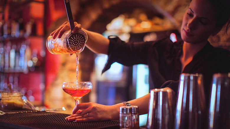 bartender pouring cocktail into coup glass