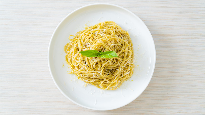 A plate of lightly seasoned spaghetti is topped with parmesan and fresh basil