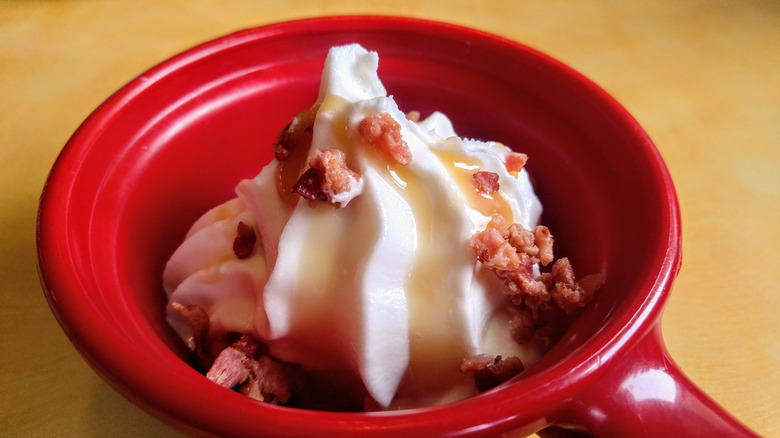 Vanilla soft serve ice cream with bacon crumbles and syrup in a red dish