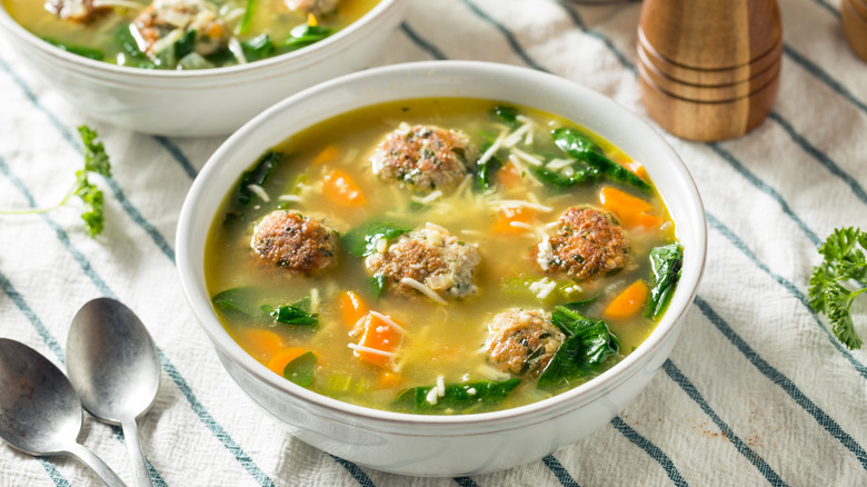 a white bowl of italian wedding soup with fresh herbs on a table