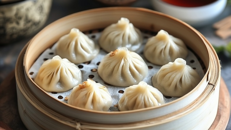 Eight soup dumplings sit in a bamboo steamer