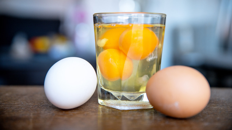 Raw eggs in a glass surrounded by two eggs