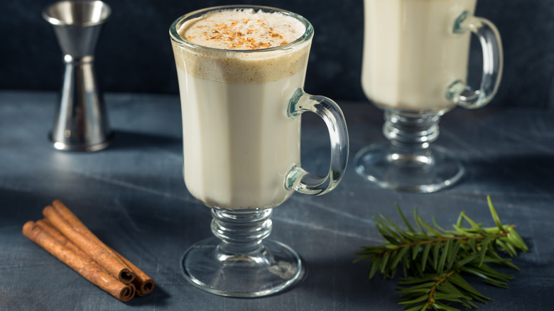 Glass of a Tom & Jerry holiday cocktail with cinnamon sticks