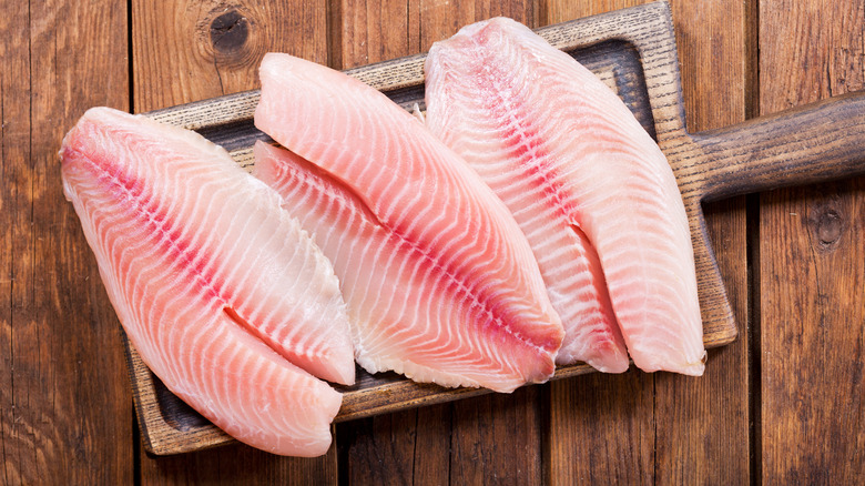 Three raw fish fillets with the nape removed sit on a wooden cutting board