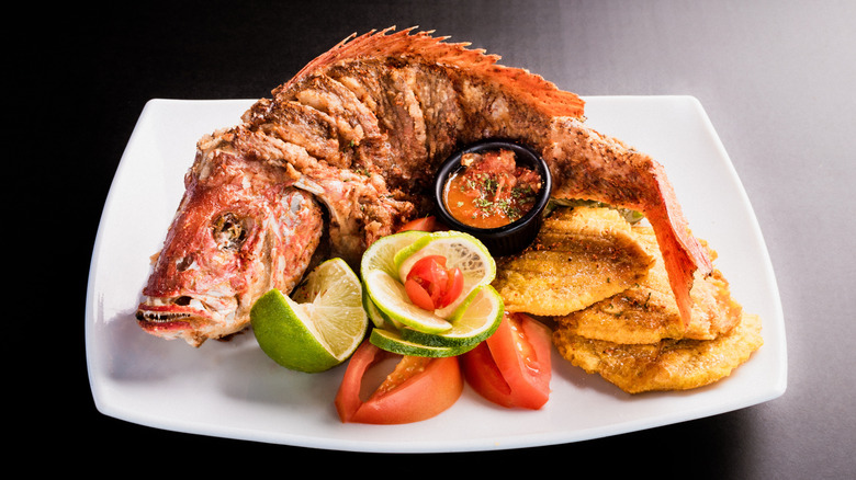 A whole fried snapper is presented on a plate with sides.