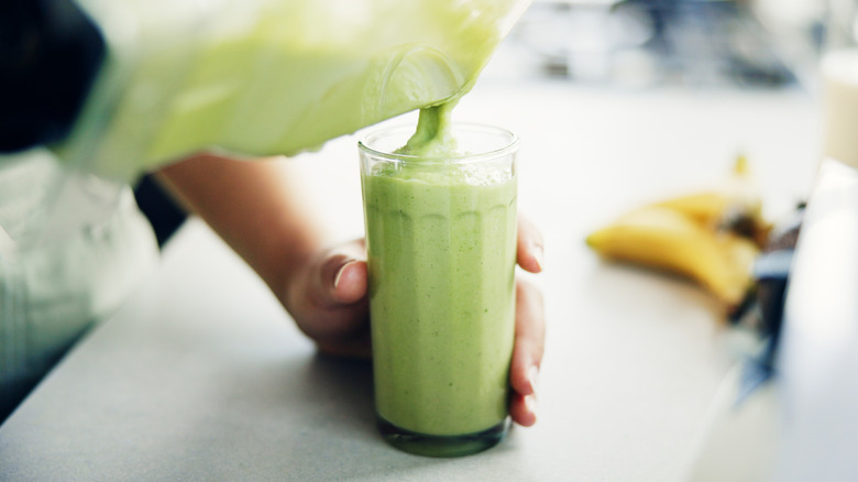 A green shake is poured from a blender into a clear drinking glass