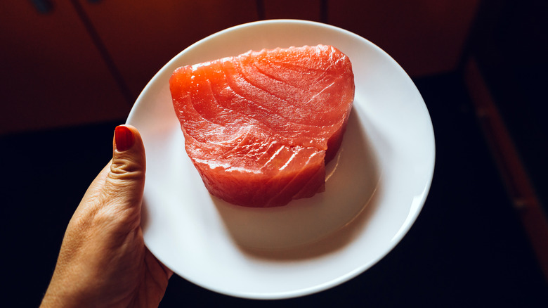 Hand holding plate of raw tuna steak