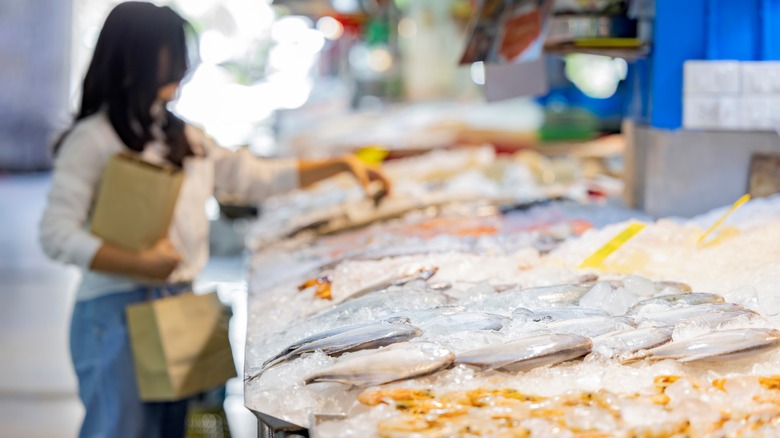 Woman selecting fish from fish counter in grocery store