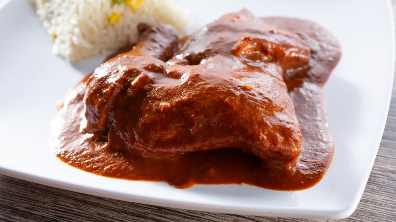 Chicken with mole colorado on white plate with rice