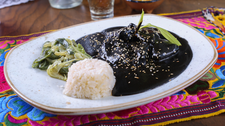 Mole negro with rice and vegetables on white plate