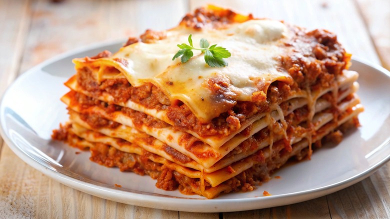 Slice of lasagna on a white plate garnished with an herb