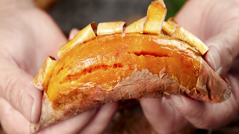 Hands peeling skin off whole roasted sweet potato