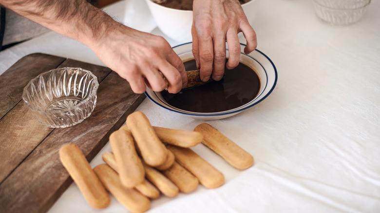 A person dipping ladyfingers in espresso liqueur.