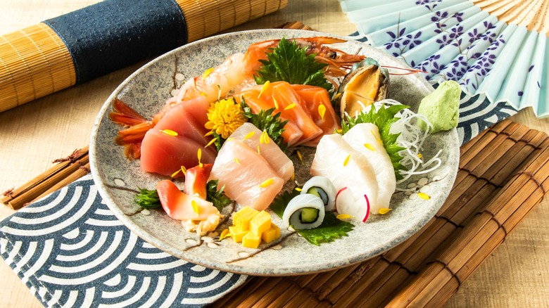 A plate of different types of sashimi including tuna and salmon, with vegetables and mango