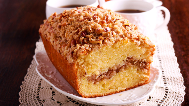 Coffee cake on a white plate with cups of coffee in the background