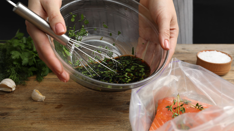 Hands pour a soy sauce and herb marinade into a bag with salmon