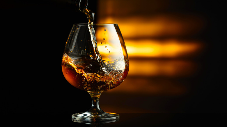 Brandy/Cognac being poured into a snifter glass with a black and gold hombre backrground