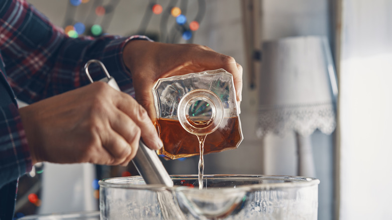 A cook pours whiskey into a mixing bowl with Christmas lights in the background