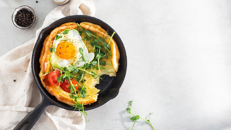Dutch baby pancake with egg, herbs, and tomatoes in skillet