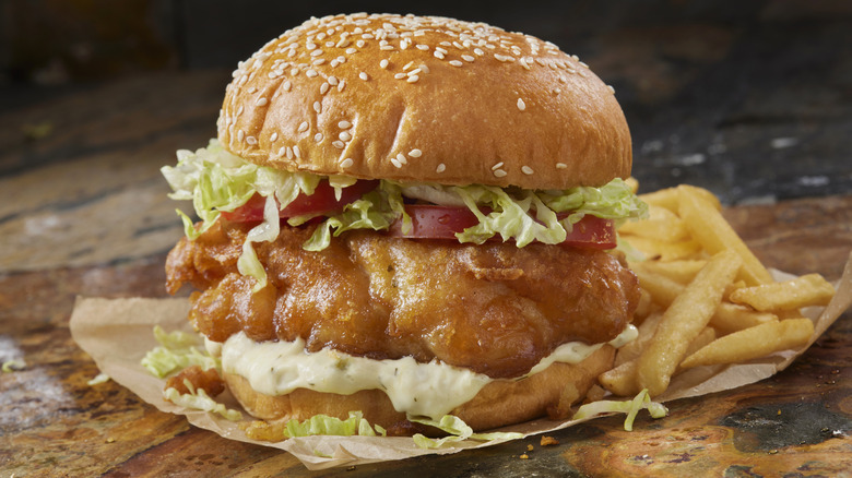 Battered fried fish sandwich with a side of fries, on paper on a wooden table