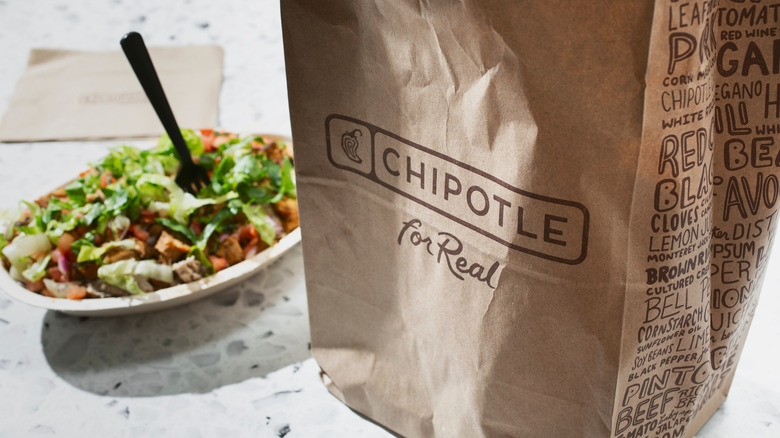 Close up of a Chipotle bag with a loaded burrito bowl in the background