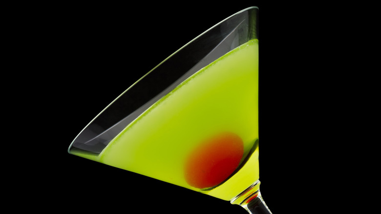 A martini glass tilts sideways, filled with Midori cocktail, the Japanese slipper, and a cocktail cherry