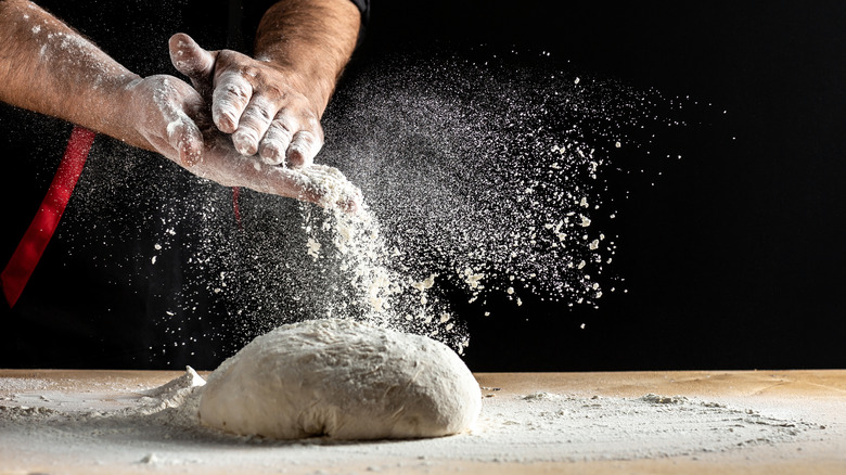 Baker powdering dough with flower