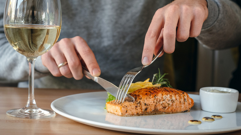 Hands cutting a salmon fillet next to glass of white wine