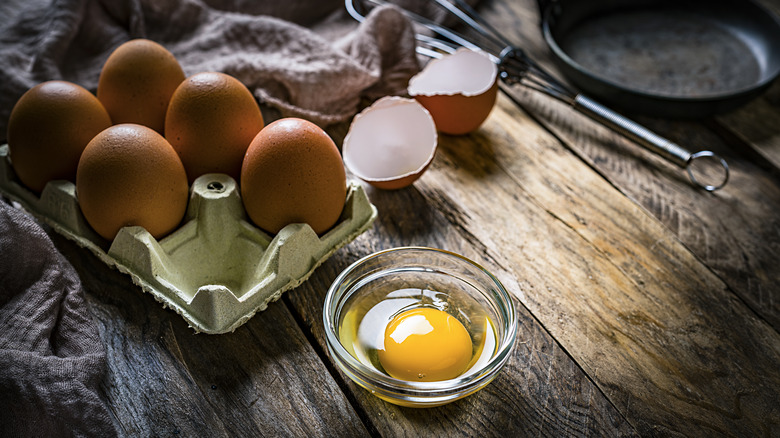 Raw egg in bowl near half dozen eggs