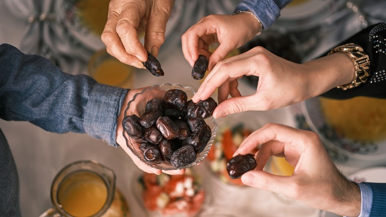 Four hands picking from bowl of dates