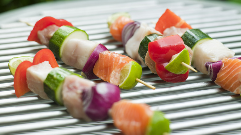 Skewers with salmon, courgette, peppers, and onions on a grill