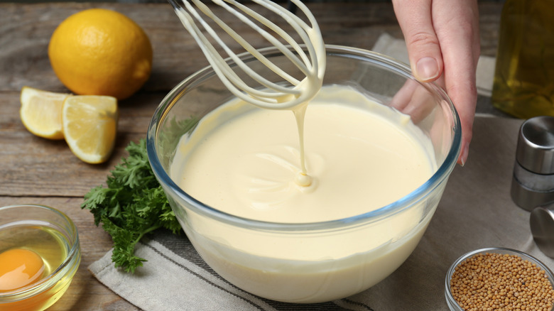 A whisk hovering over a bowl of creamy salad dressing