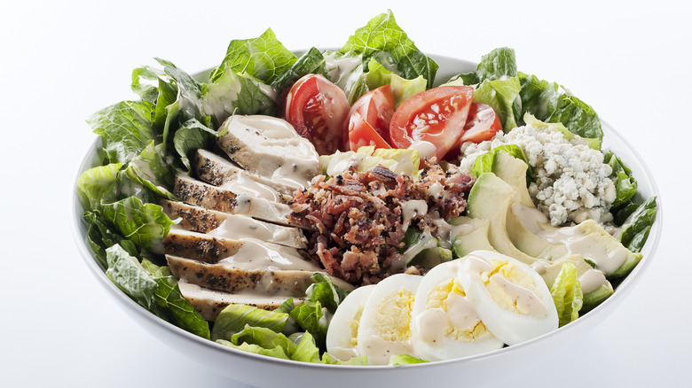 cobb salad with blue cheese on top in a metal bowl