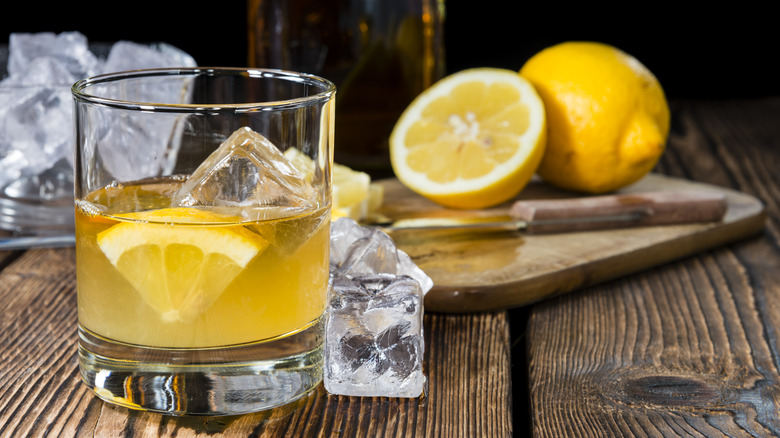 Whiskey sour cocktail in a glass with lemons on a cutting board