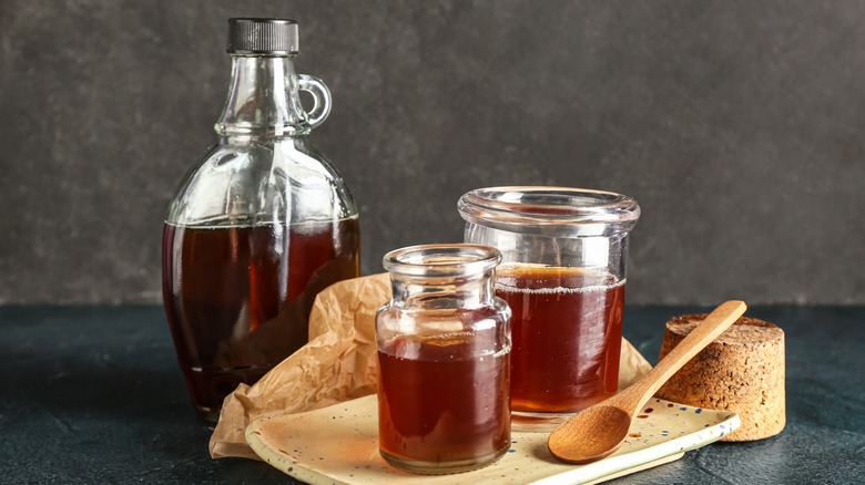 Bottle and glass jars of maple syrup with a wooden serving spoon