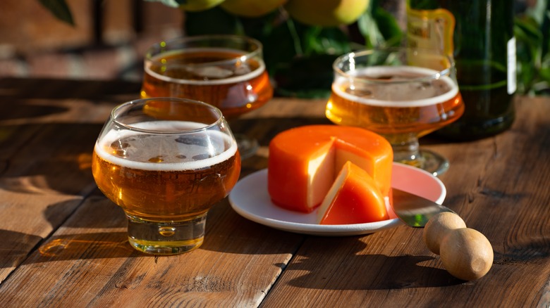 glasses of cider next to a wax-wrapped cheese