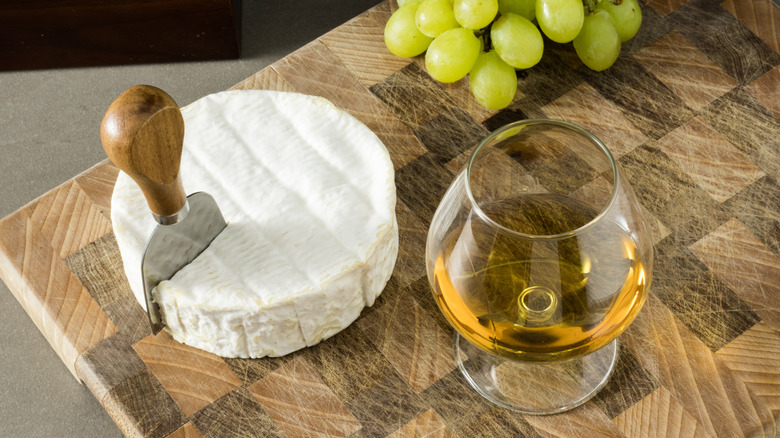 glass of Cognac and roll of brie cheese on cutting board