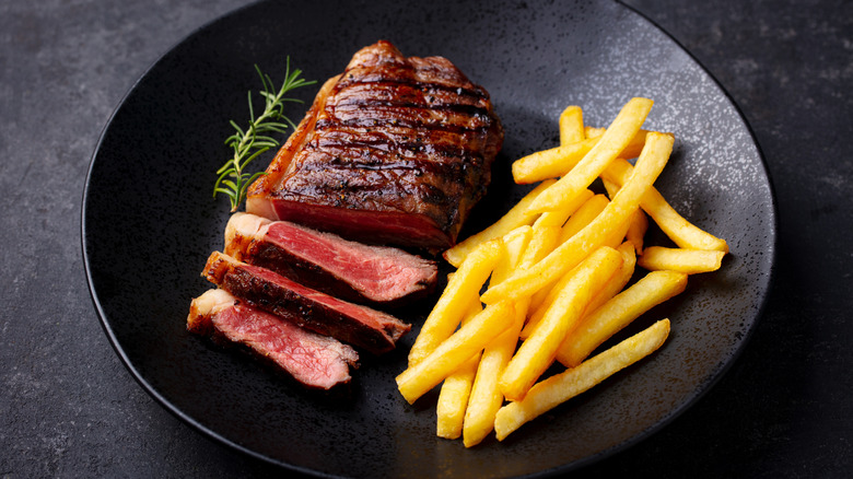 A medium-rare steak and a side of french fries sit on a black plate