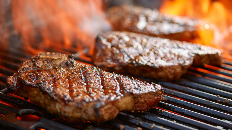 Cuts of strip loin steak sit on a hot grill while being cooked