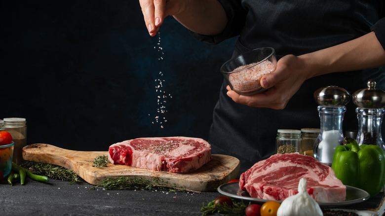 Sprinkling salt onto raw ribeye steaks before cooking